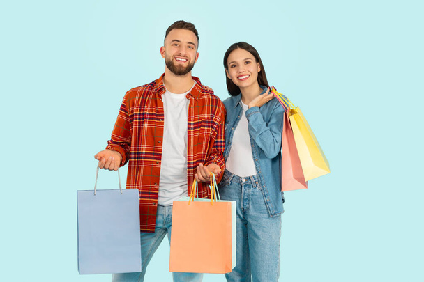 Nakupování a prodej. Spokojeni mladí pár Zákazníci, kteří drží mnoho balíčků s nákupy, těší slevy na černý pátek, stojící na modrém pozadí studia - Fotografie, Obrázek