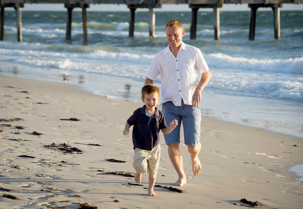 happy father playing on the beach with little son running excited with barefoot in sand and water - Photo, Image