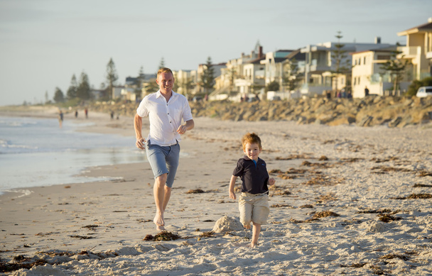 feliz padre jugando en la playa con su pequeño hijo corriendo excitado con los pies descalzos en la arena y el agua
 - Foto, imagen