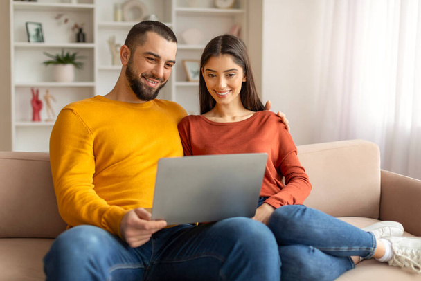 Technológiák a kikapcsolódásra. Boldog fiatal pár használja Laptop együtt otthon, mosolygó kaukázusi házastársak pihentető kanapén számítógép, nézés filmek vagy böngészés internet, szabad tér - Fotó, kép