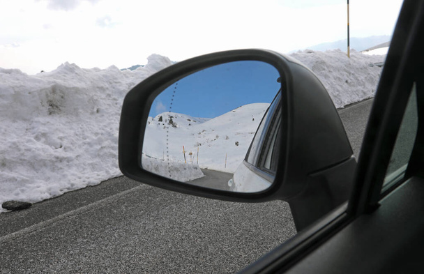 Καθρέφτης οπισθοπορείας του επιβατικού αυτοκινήτου στον ορεινό δρόμο το χειμώνα με χιόνι και αντανάκλαση του παρελθόντος - Φωτογραφία, εικόνα