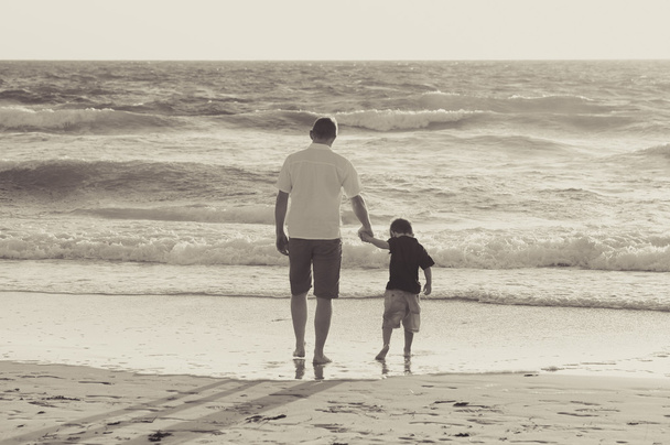 feliz padre sosteniendo de la mano del pequeño hijo caminando juntos en la playa con descalzo
 - Foto, imagen
