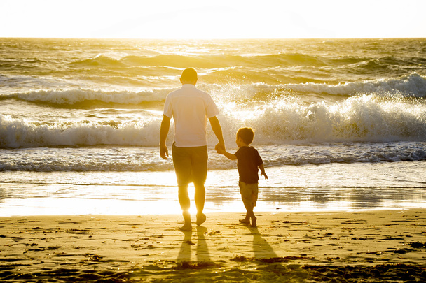 glücklicher Vater hält Händchen mit kleinem Sohn, der barfuß am Strand spaziert - Foto, Bild