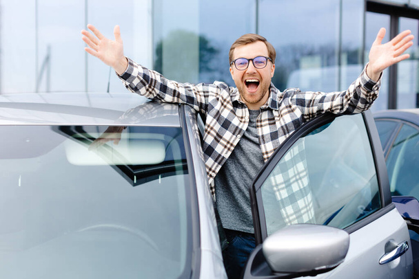 Iloinen kaveri seisoo lähellä autoand hymyillen, ostaa auton jälleenmyyntikeskuksessa - Valokuva, kuva