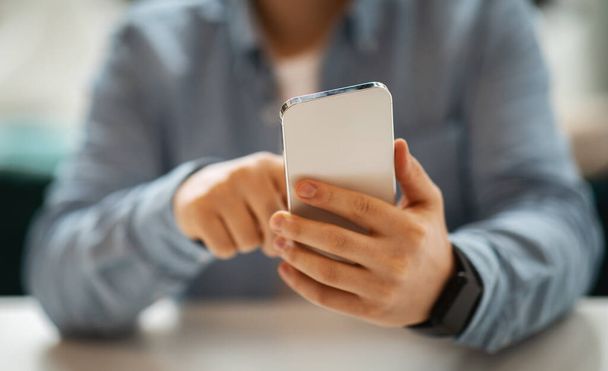 Κοντινό πλάνο του καυκάσιου χέρια mans χρησιμοποιώντας ένα smartphone, εστιάζοντας στην οθόνη με ένα θολό φόντο, προβάλλοντας σύγχρονη τεχνολογία επικοινωνίας κατά τη χρήση app, συσκευή, περικοπεί - Φωτογραφία, εικόνα