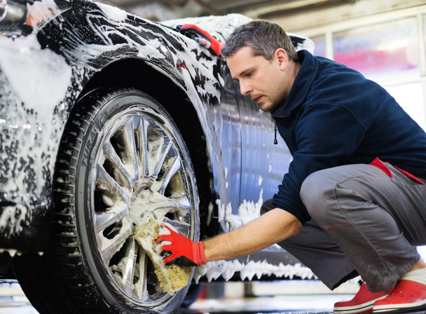 Hombre trabajador lavando ruedas de aleación de coche en un lavado de coches  - Foto, Imagen