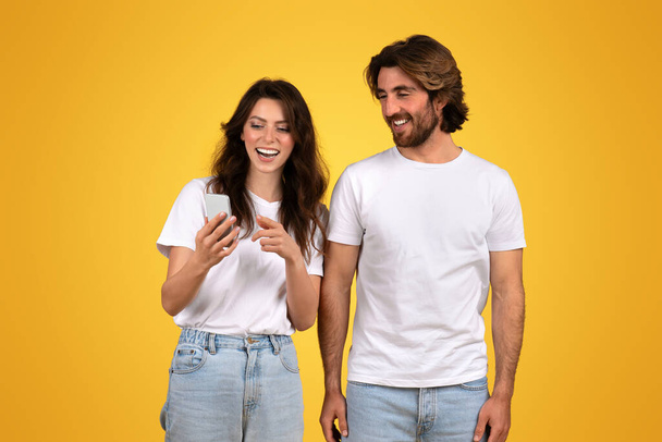 Молодая европейская пара совместно использует ноутбук, показывая командную работу и общий цифровой опыт на привлекательном желтом фоне, студию - Фото, изображение