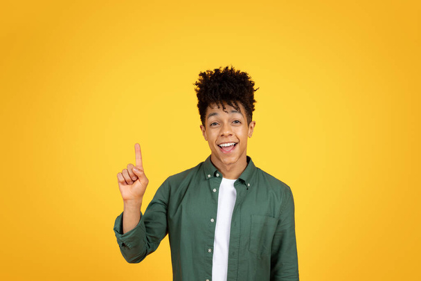 Inspirado chico afroamericano milenario levantando el dedo y exclamando, tienen una gran idea creativa, aislado en el fondo del estudio amarillo, espacio de copia - Foto, imagen