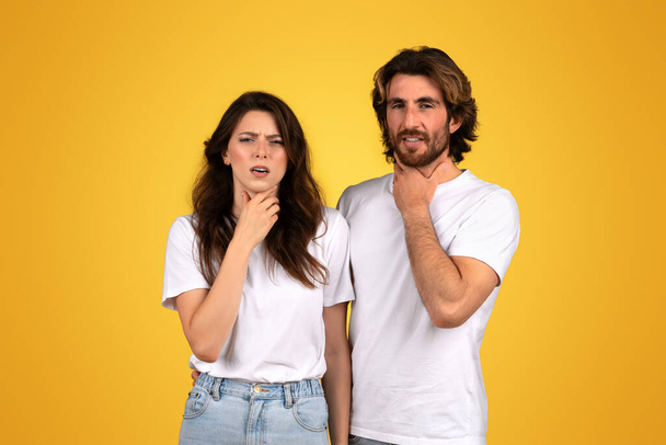Zmatený nešťastný bělošský pár s ustaranými výrazy, žena s rukou na bradě a muž dotýkající se jeho krku, oba v bílých košilích na žlutém pozadí, studio - Fotografie, Obrázek