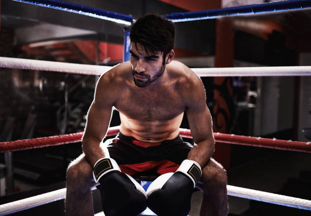 MMA, boxer and man sitting in ring ready for challenge, competitive and confident from training in gym. Male person, healthy and fitness from practice in exercise studio as athlete and fighter. - Photo, Image