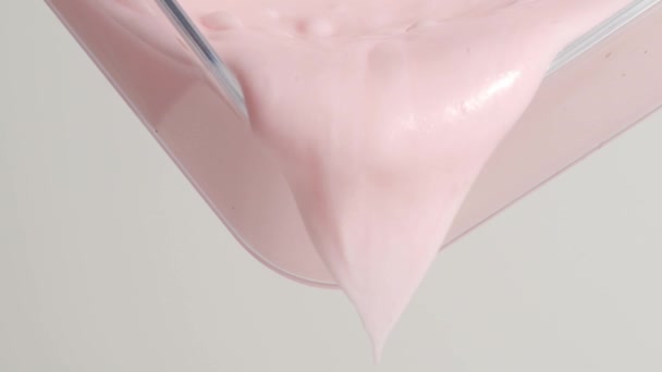 Substância cremosa rosa pálida grossa transborda suavemente da borda de uma bandeja transparente. - Filmagem, Vídeo