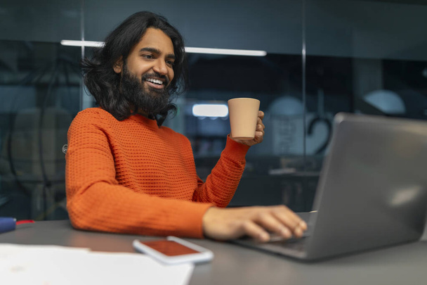 Lächelnder Profi mit einem angenehmen Moment, während er am Schreibtisch mit seinem Computer interagiert - Foto, Bild