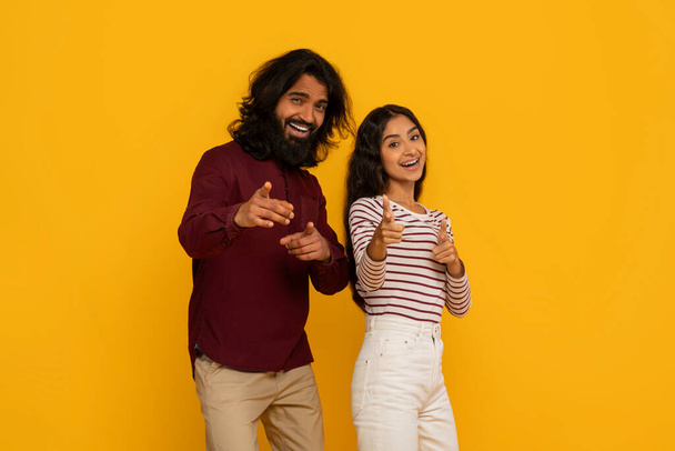 Una pareja comprometida apunta directamente al espectador, sus expresiones animadas sugieren una llamada interactiva a la acción en amarillo - Foto, imagen