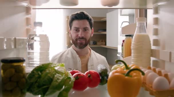 Pohled zevnitř lednice POV kavkazský muž majitel domu otevřený lednice dveře kuchyně plná produktů jídlo usměvavý najít vzít červené rajče šťastný úsměv vaření salát zdravý vegetarián - Záběry, video