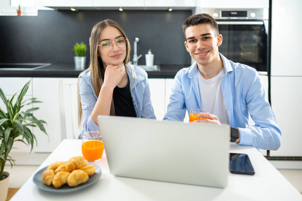 Portrait of teenage girl and boy in smart casual clothes sitting at desk with laptop and drinking juice at home - Photo, Image