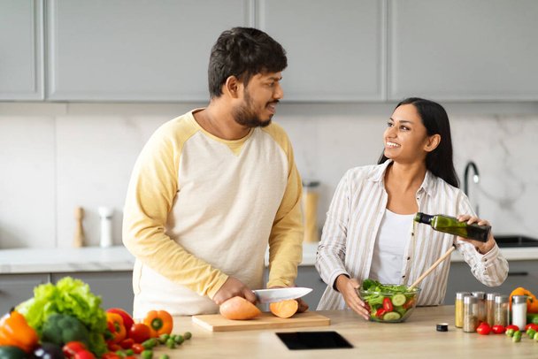 Feliz joven pareja vegetariana india cocinando juntos en casa. Positivo oriental hombre y mujer cónyuges preparando comida saludable en la acogedora cocina moderna, tener conversación, espacio de copia - Foto, Imagen