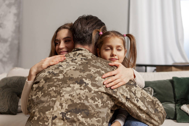 military man of the Ukrainian army in camouflage uniform returned home and hugs his family, soldier goes to war and says goodbye to his daughter and wife, the concept of mobilization in Ukraine - Photo, Image