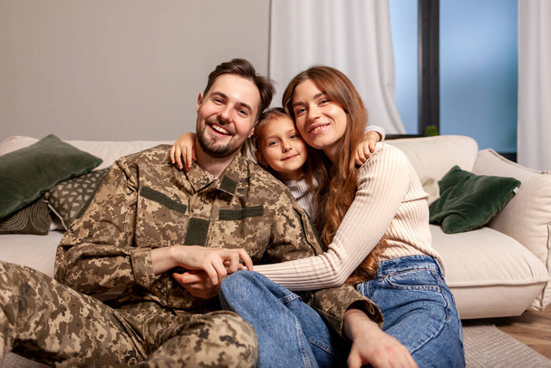 militaire man van het Oekraïense leger in camouflage uniform keerde terug naar huis en knuffelt zijn familie, soldaat gaat naar de oorlog en neemt afscheid van zijn dochter en vrouw, het concept van mobilisatie in Oekraïne - Foto, afbeelding