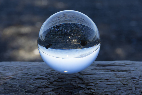 Una bola de lente de cristal que refleja la imagen de una playa rocosa justo después del atardecer.  - Foto, Imagen