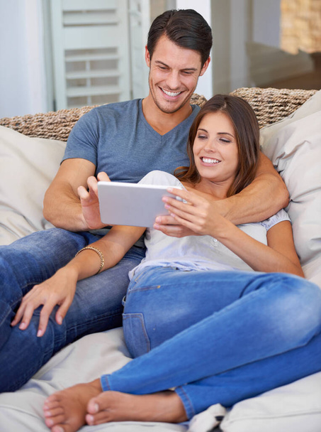 Happy couple, hug and sofa with tablet for entertainment, movie or social media at home. Man and woman lying in relax with smile on technology for online streaming, series or show in living room. - Photo, Image