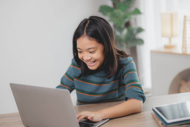Een jong meisje zit achter een bureau met een laptop en een tablet. Ze lacht en ze geniet van haar tijd. - Foto, afbeelding