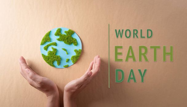 Hands holding paper earth with grass on brown background. World environment day, earth day and save earth concept. - Photo, Image