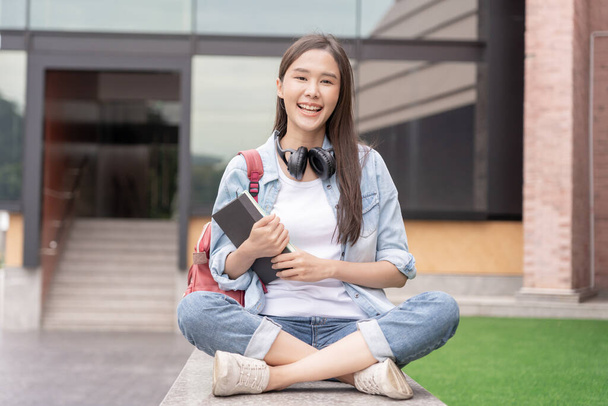 Piękna studentka azjatycka kobieta z plecakiem i książkami na zewnątrz. Uśmiechnięta dziewczyna z dużą ilością książek w kampusie. Portret kobiety na Międzynarodowym Uniwersytecie Azji. Edukacja, nauka, szkoła - Zdjęcie, obraz