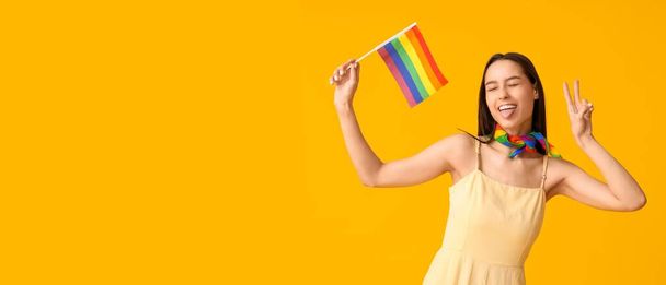 Όμορφη νεαρή γυναίκα με σημαία ΛΟΑΤ δείχνει χειρονομία νίκης σε κίτρινο φόντο με χώρο για κείμενο - Φωτογραφία, εικόνα