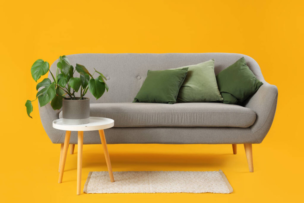 Moderne Wohnzimmereinrichtung mit grauem Sofa, Kissen und Tisch auf gelbem Hintergrund - Foto, Bild
