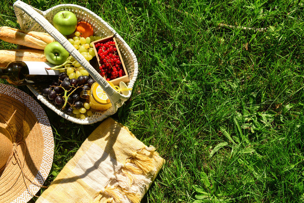 Manta, sombrero y canasta de mimbre de sabrosa comida con bebidas para picnic romántico en la hierba en el parque - Foto, Imagen