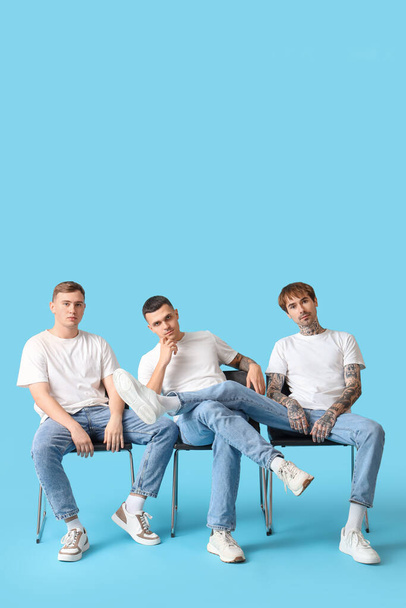 Young men in stylish jeans sitting on blue background - Фото, изображение