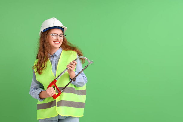 Trabajadora de la construcción en gafas con sierra de hackear sobre fondo verde - Foto, Imagen