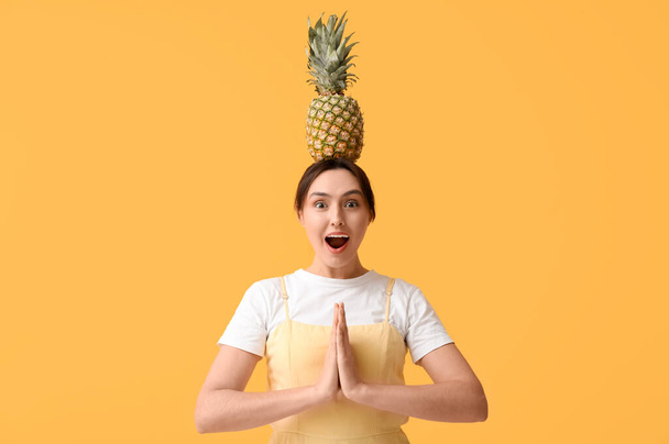 Beautiful young woman with fresh pineapple on her head on yellow background - Photo, Image
