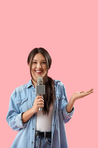 Female Asian journalist with microphone talking on pink background - Photo, image