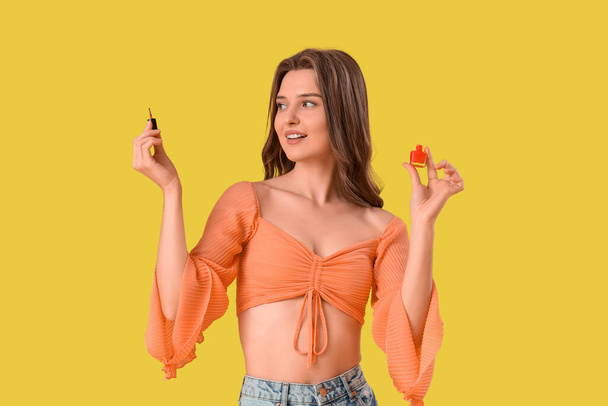 Młoda kobieta z butelką lakieru do paznokci na żółtym tle - Zdjęcie, obraz