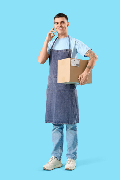 Male online store seller with parcel talking by mobile phone on blue background - Photo, Image