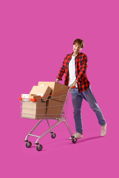 Junger Online-Verkäufer mit Warenkorb von Paketen auf lila Hintergrund - Foto, Bild