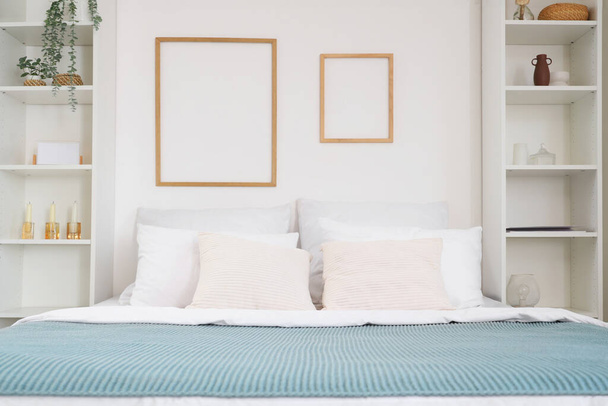 Interno di camera da letto luminosa con grande letto, mensole e cornici - Foto, immagini