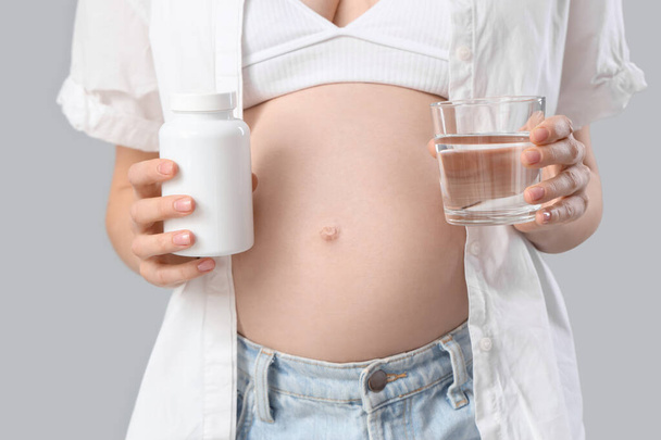 Junge schwangere Frau mit Tablettenflasche und Glas Wasser auf hellem Hintergrund, Nahaufnahme - Foto, Bild