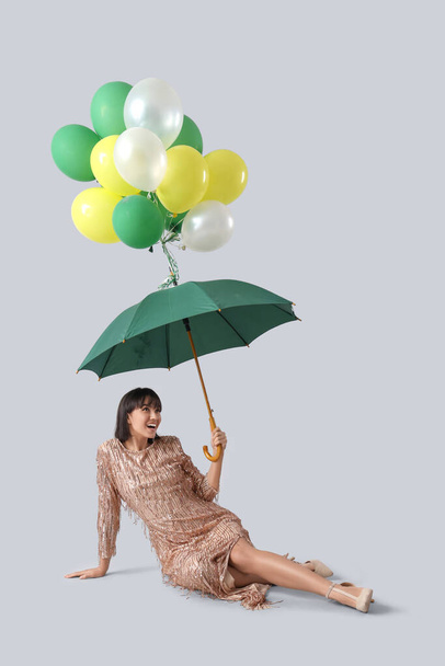Όμορφη νεαρή γυναίκα κρατώντας ομπρέλα με μπαλόνια στο φως φόντο - Φωτογραφία, εικόνα