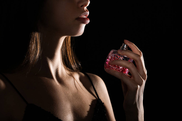 Siyah arka planda güzel bir parfüm şişesi olan güzel bir kadın. - Fotoğraf, Görsel