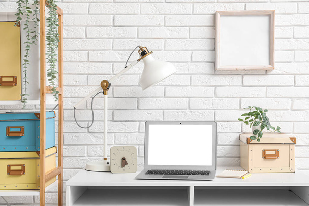 Стильне робоче місце з ноутбуком біля білої цегляної стіни - Фото, зображення