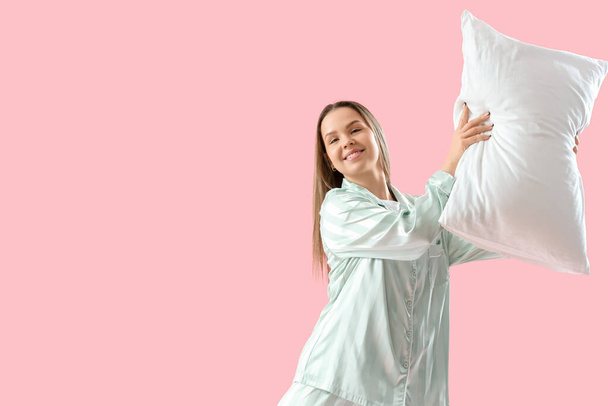 ピンクの背景に柔らかい枕を持つパジャマの若い女性 - 写真・画像