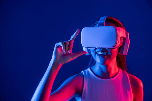 Vrouwelijke staande omringd door neon licht dragen VR-headset aansluiten metaverse, futuristische cyberspace community technologie, verspreiden index en duim vinger interactie virtueel object. Hallucinatie. - Foto, afbeelding