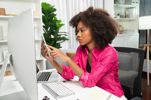 Genç Afrikalı iş kadını projesini ekran monitörü laptopuna odaklıyor, web sitesi bilgisayarındaki veri merkezini ve akıllı telefonu araştırıyor. Mekan teması sade renkte rahat bir odada çalışır. Tatlandırıcı. - Fotoğraf, Görsel