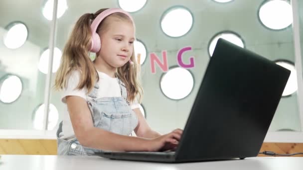 Nuori opiskelija työskentelee kannettavan tietokoneen tai opiskelee verkossa luokkahuoneessa. Valkoihoinen tyttö kirjoittamalla kannettavan samalla kotitehtäviä tai kuuntelemalla musiikkia.Pieni lapsi yllään kuulokkeet. Luova oppiminen. Virheellisyys. - Materiaali, video