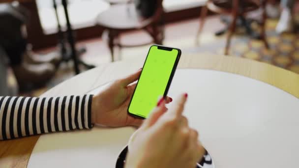 Genç bir kadın kahve dükkanında kahve içiyor ve telefonda çalışıyor. Kadın, telefon ekranını sarıyor. Telefonda yeşil ekran. Serbest konsept 4K - Video, Çekim