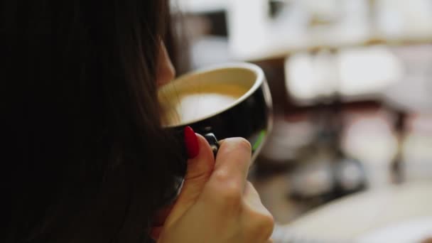 Mujer joven bebe café en una cafetería y trabaja en el teléfono. Freelancer femenina pasa la pantalla del teléfono. Pantalla verde en el teléfono. Concepto independiente 4k - Metraje, vídeo