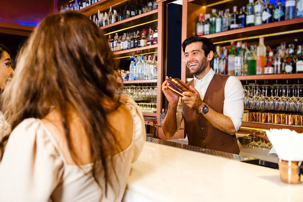 Kavkazský profesionální barman nebo mixolog, který připravuje koktejl pro ženy v baru. Atraktivní barman mísí likéry s koktejlovým koktejlem s úsměvem. Barman v nočním klubu restaurace. - Fotografie, Obrázek