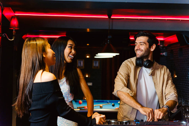 Group of energetic women dancing friends with DJ enjoying night party. Young women dance and hold a wine glass in nightclub. Nightlife, disco dance and girl's night party concept. Fun music festival - Photo, Image